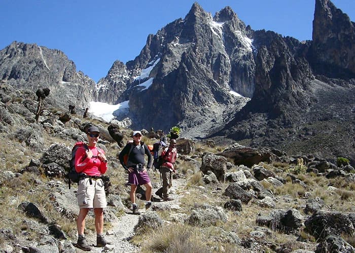 Four trekkers with backpacks and trekking poles crossing open mountain terrain