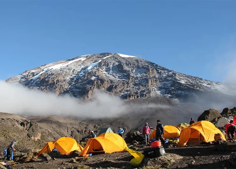Dome tents and trekkers at a rocky mountain camp below steep terrain
