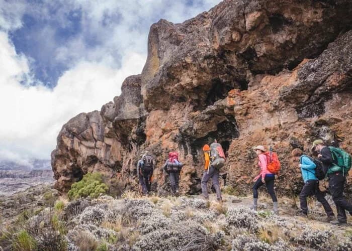 Trekkers walking below a large rock outcrop beneath cloud