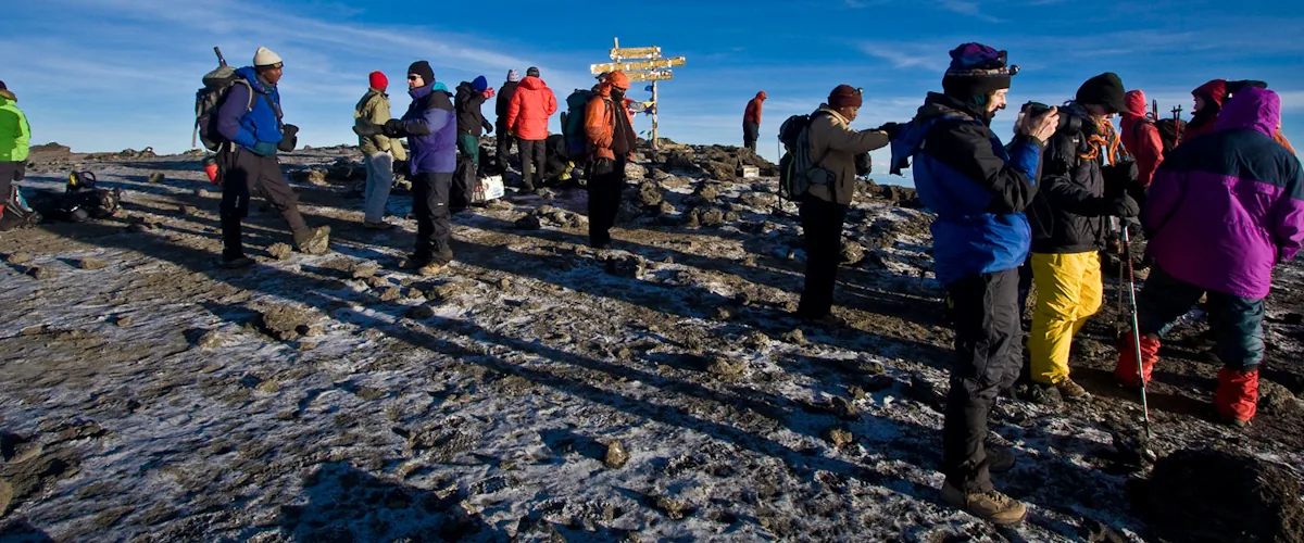 Trekkers crossing rocky high-altitude terrain beside a route sign